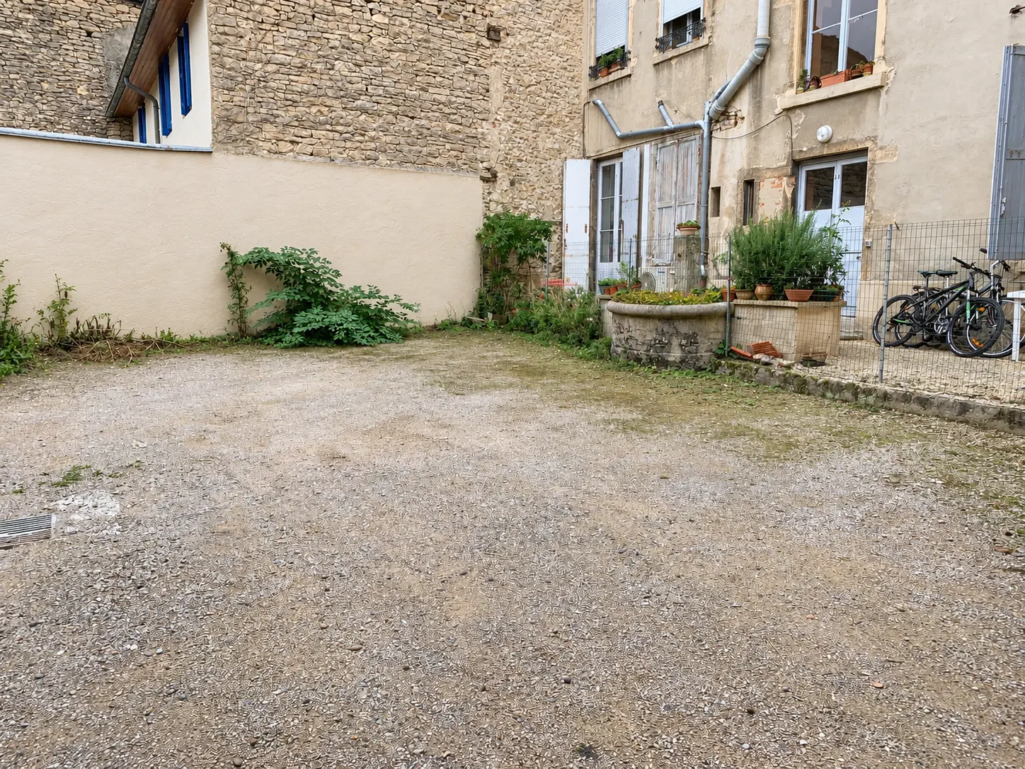 Cour intérieure de la propriété — sol en gravier, mur en pierre et puits fleuri